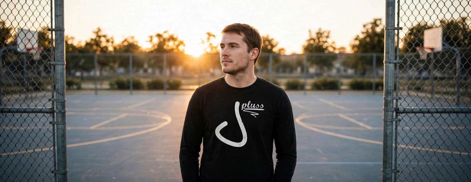 Man leaning on a chain-link fence wearing the black Jay Pluss logo long sleeve